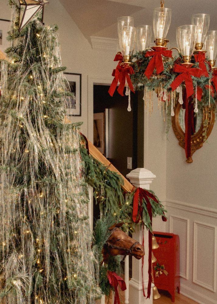 A flocked tree and garlanded staircase beneath a chandelier with red bows