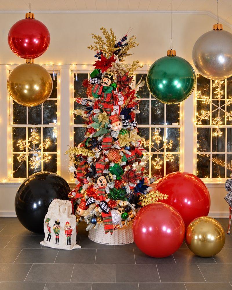 A tree with oversized red, gold, green and black ornaments before lit windows