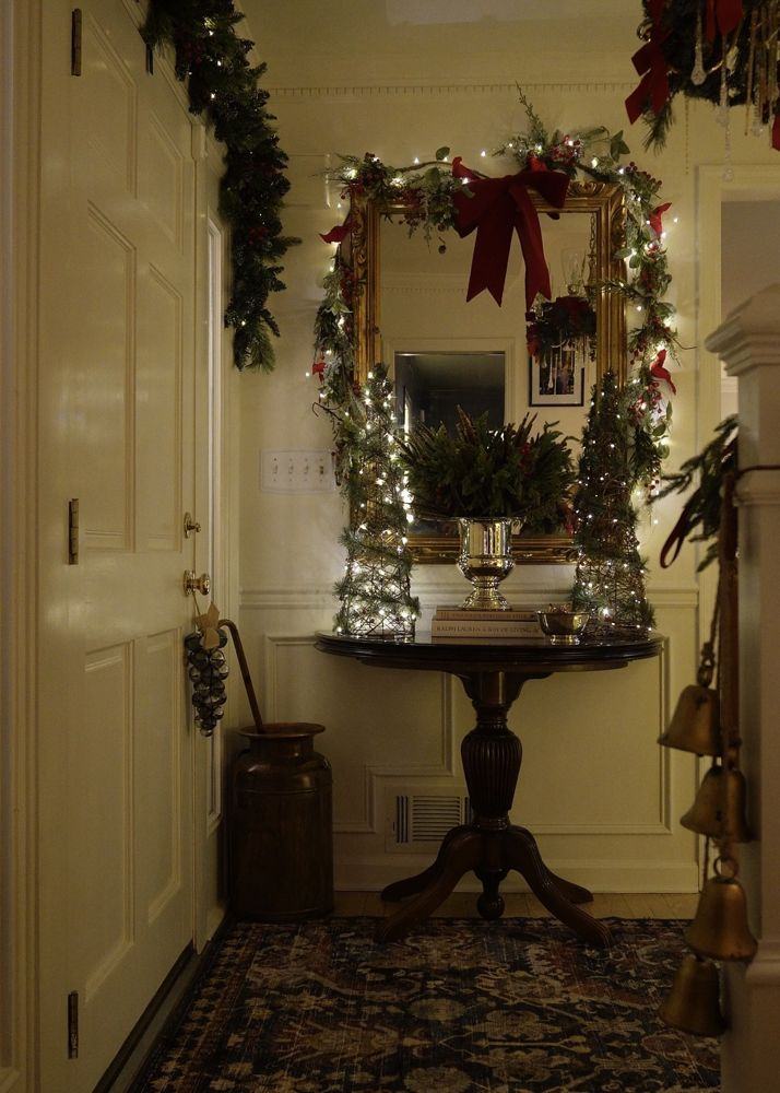 A front hall console with a garland-framed mirror and red velvet bow