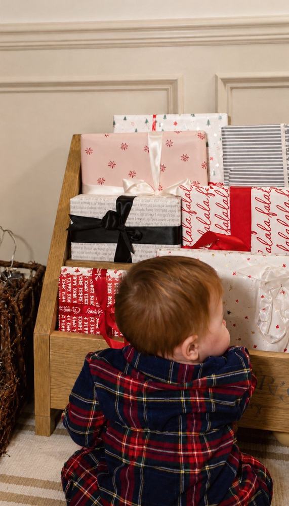 A little boy in tartan pajamas sitting in front of a shelf of wrapped Advent books