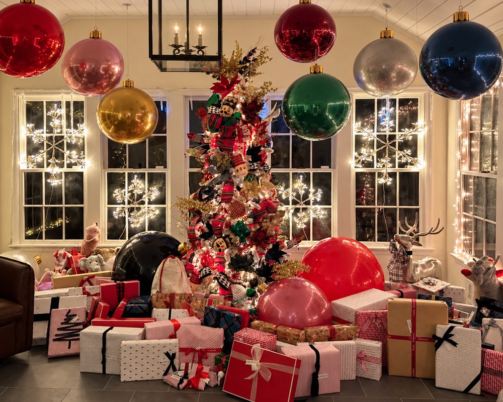 A sunroom at night with giant ornaments hanging overhead, a decorated tree and dozens of wrapped gifts in striped, kraft and white paper with red and black ribbon