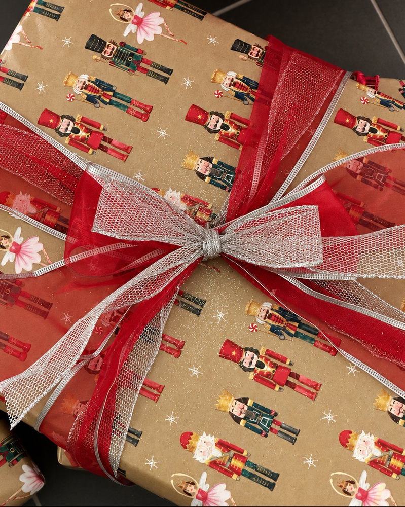A gift in kraft nutcracker paper tied with red organza and silver mesh ribbon