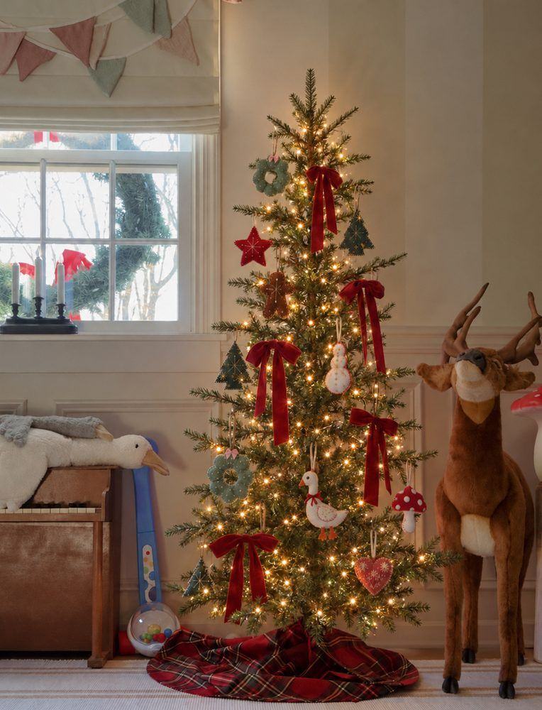 A child’s tree decorated with red velvet bows and felt ornaments, a plush reindeer standing beside it