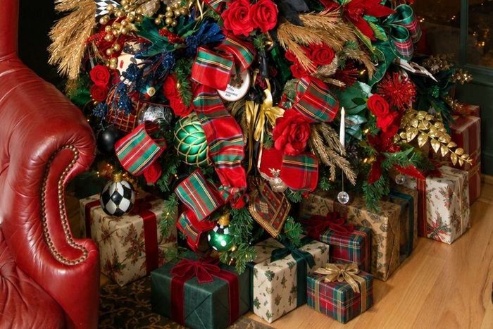 Wrapped gifts in tartan and holly paper arranged beneath a decorated tree